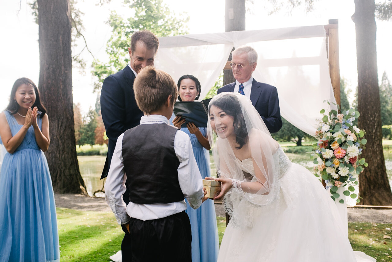  Bride under veil takes rings from ring bearer and smiles 