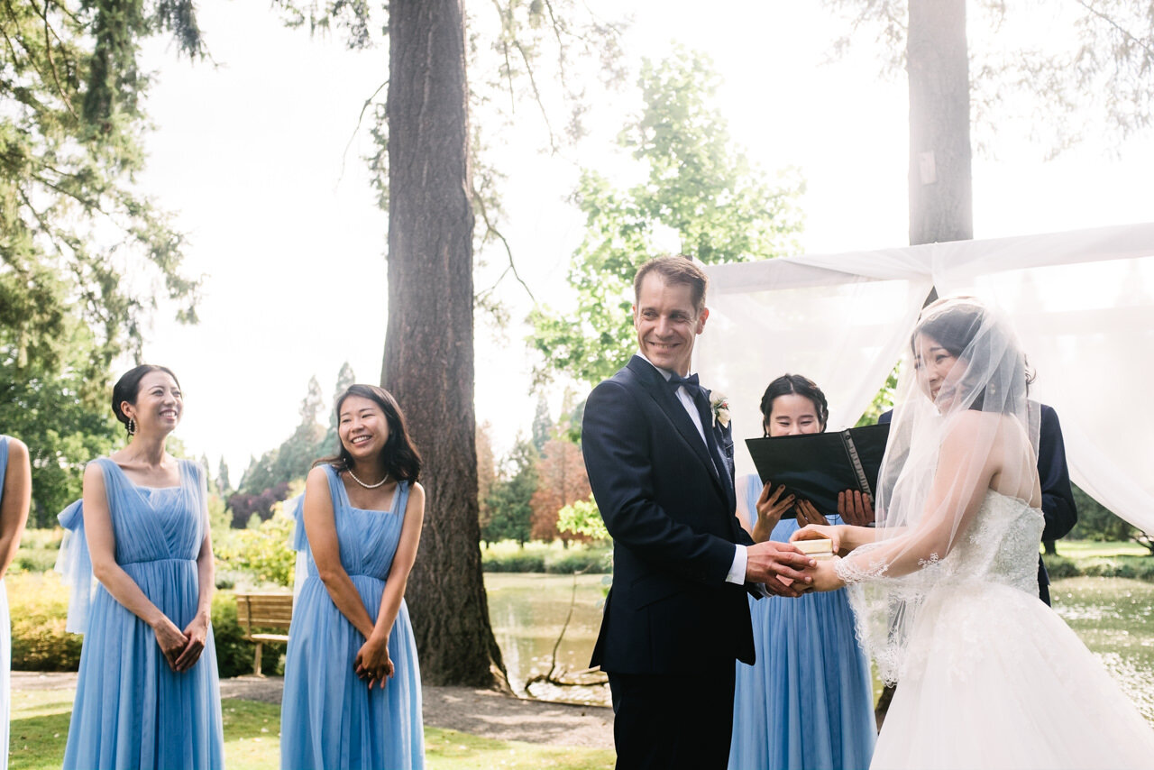  Groom and bride laugh while holding ring box in front of fir trees 