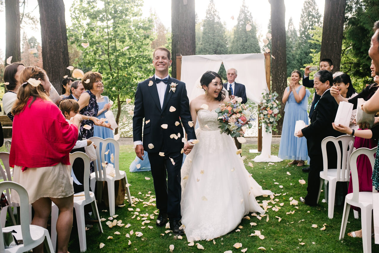  Bride and groom walk together while guests toss peach rose pedals walking down wedding aisle at crystal springs 