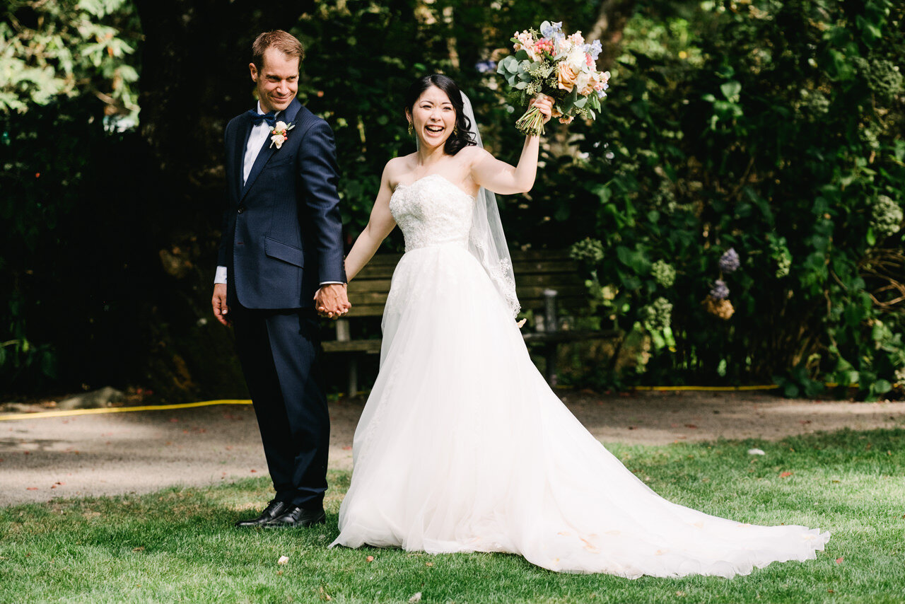  Bride smiles and holds up large peach and blue bouquet before leaving wedding ceremony 