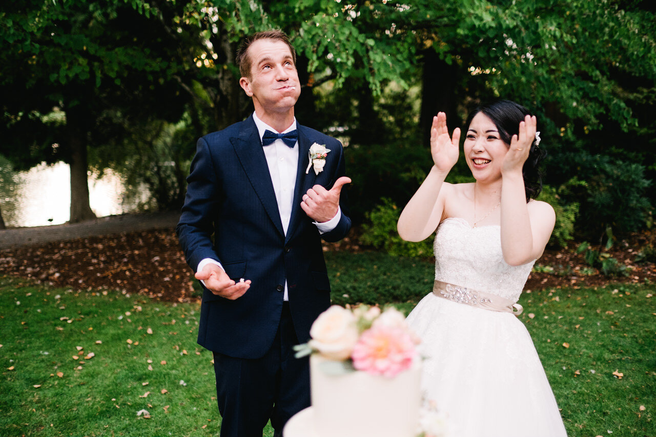  Groom gives thumbs up to wedding cake while japanese bride claps 