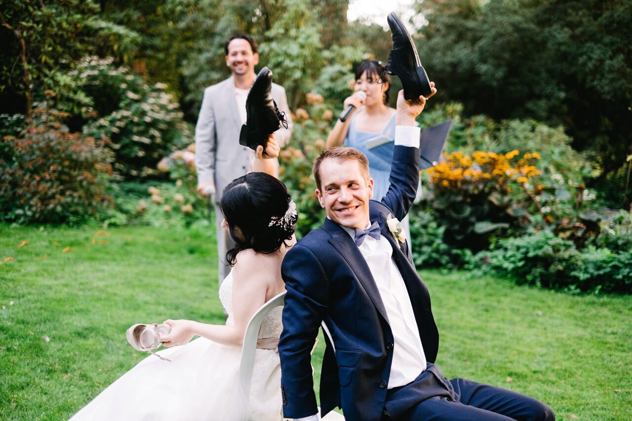  Groom and bride sitting opposite in chairs hold up shoes 