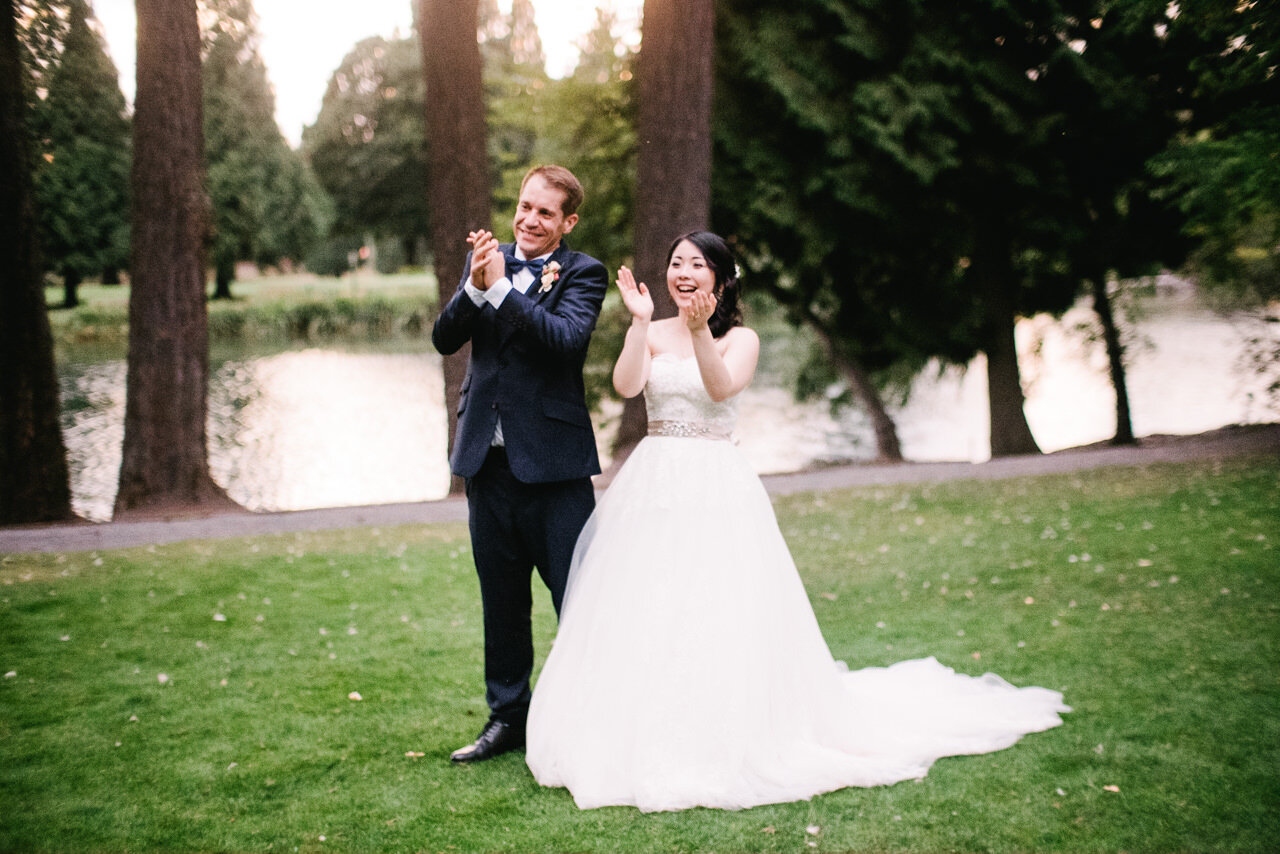  Bride and groom clap standing together on reception lawn during sunset toasts 