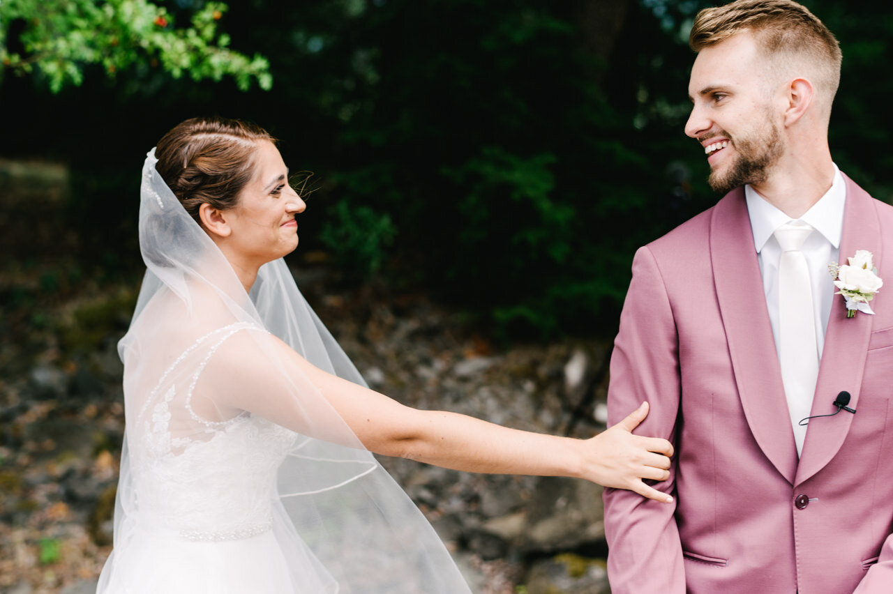  Bride in veil reaches out to groom in purple suit during first look 