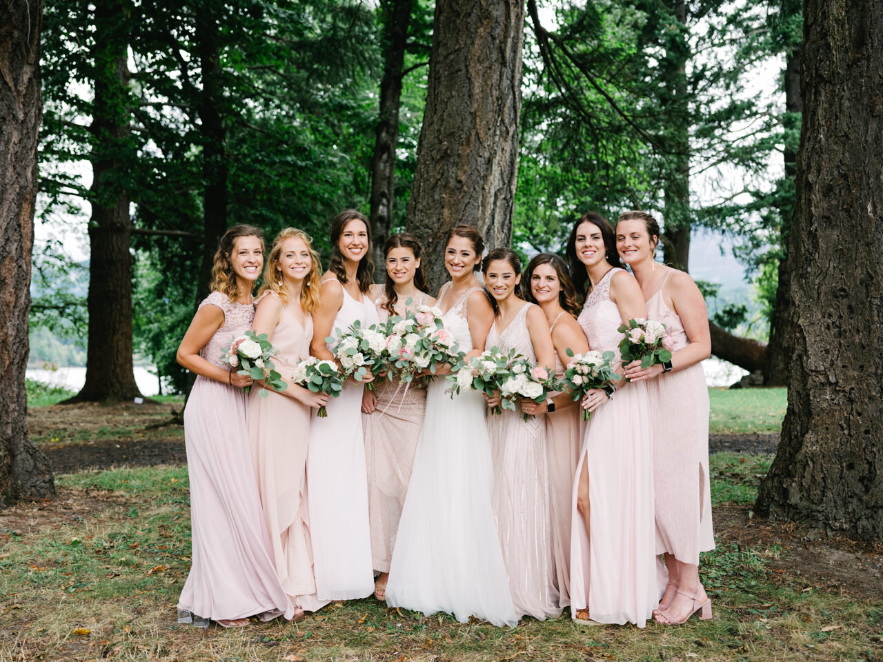  Bride and bridesmaid portrait in large fir trees, with bridesmaids dressed in peach and pink 