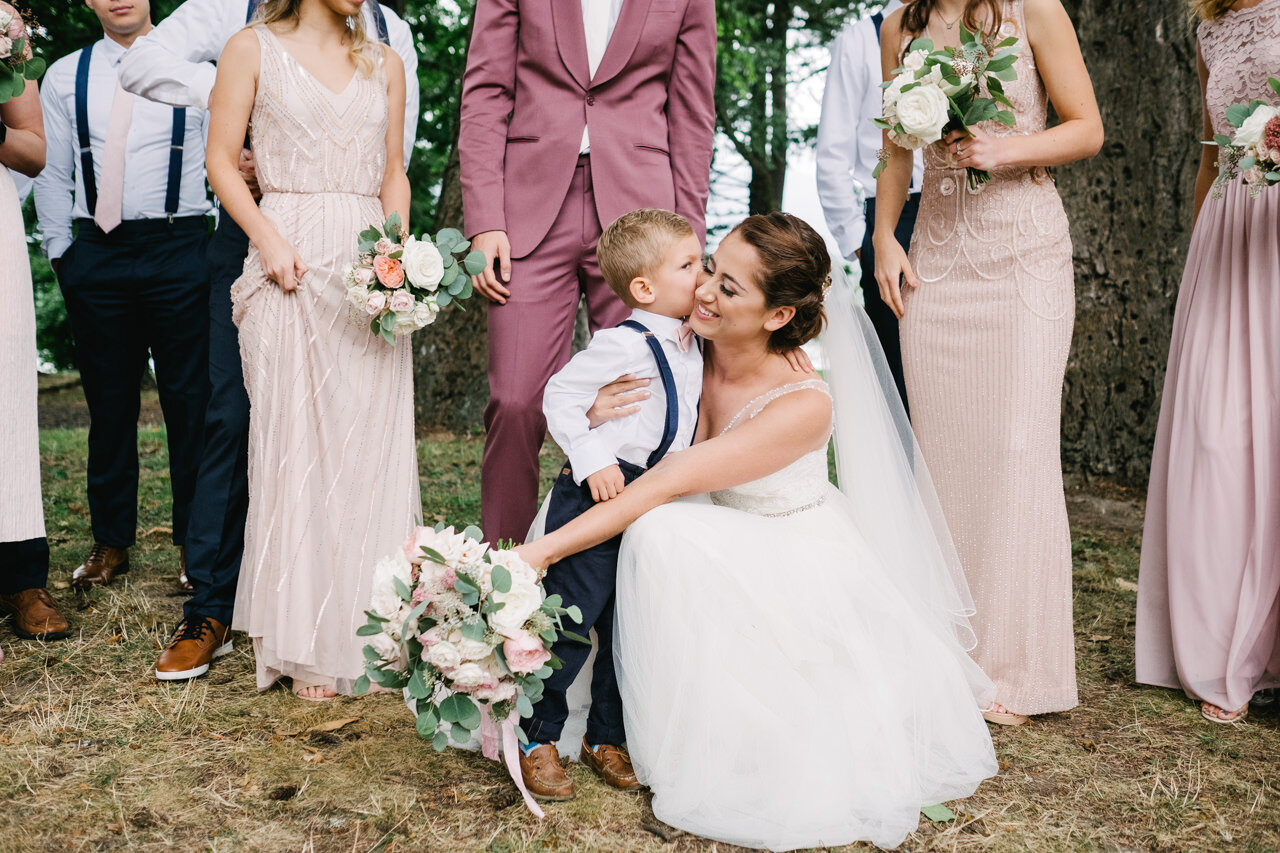  Candid moment of ring bearer kissing the bride crouched down during wedding photos 
