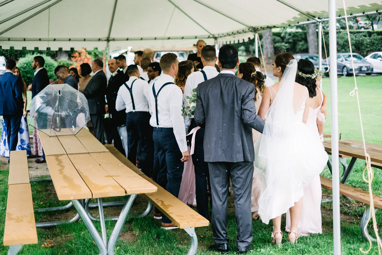  Bride stands with father under tent with processional line 