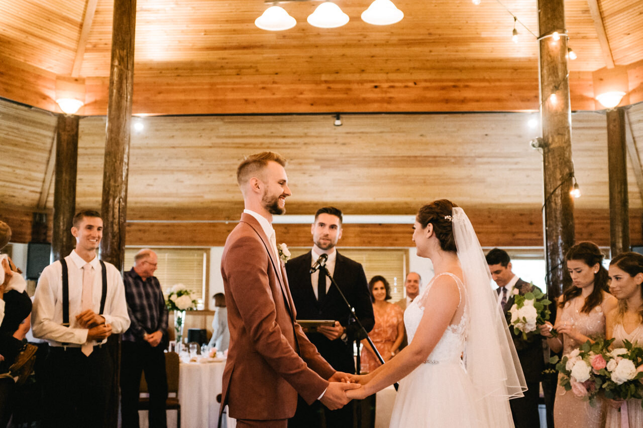  Groom smiles at bride during wedding ceremony in indoor pavilion at cascade locks 