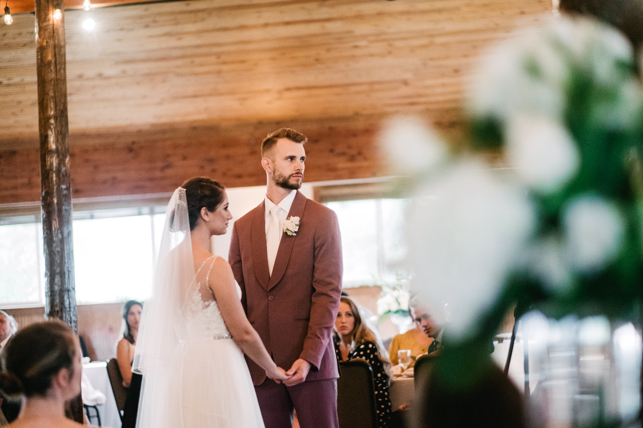  Bride and groom listen to wedding officiant with white florals in foreground 