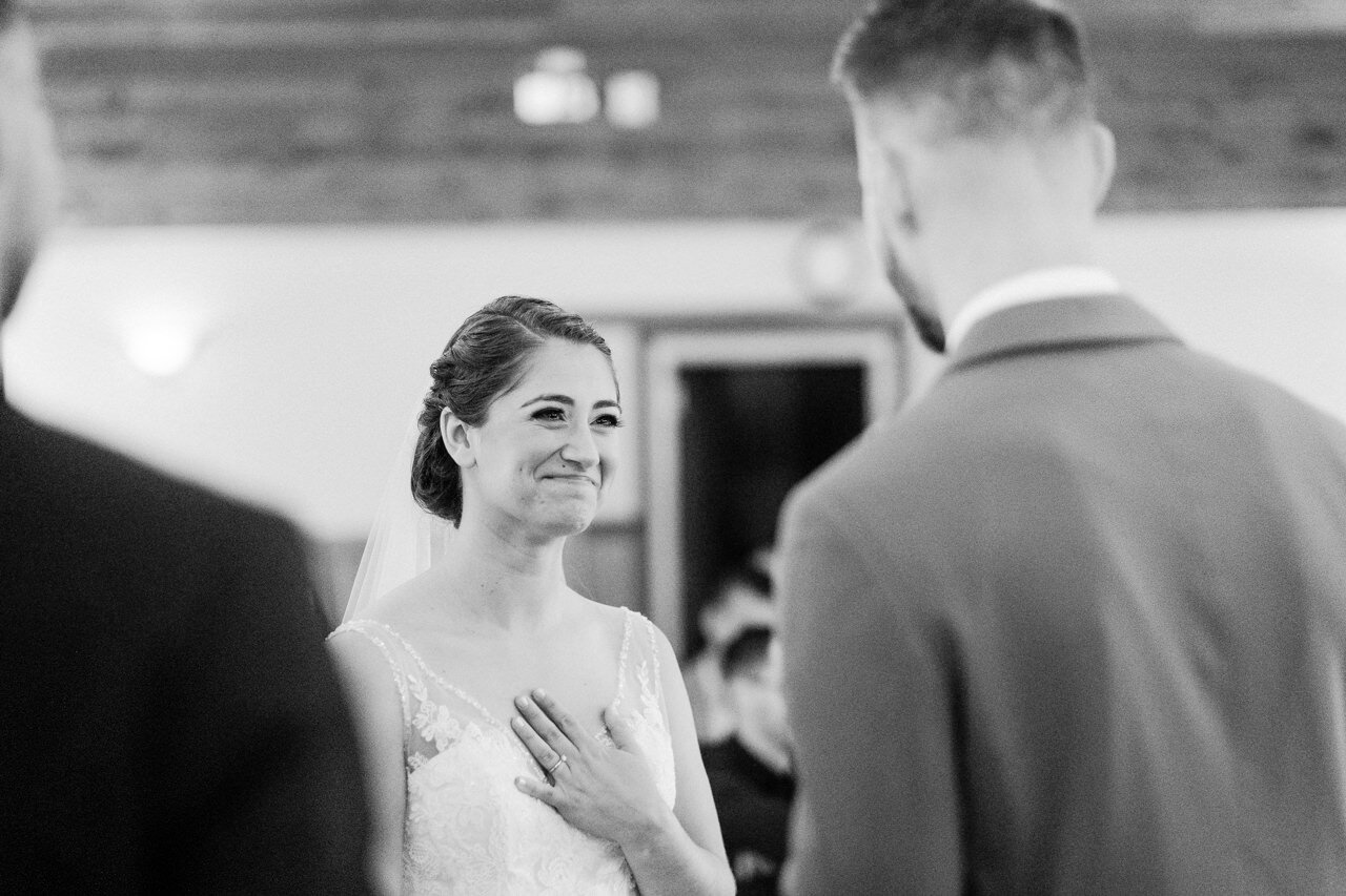  Bride holds her heart and smiles during wedding vows 