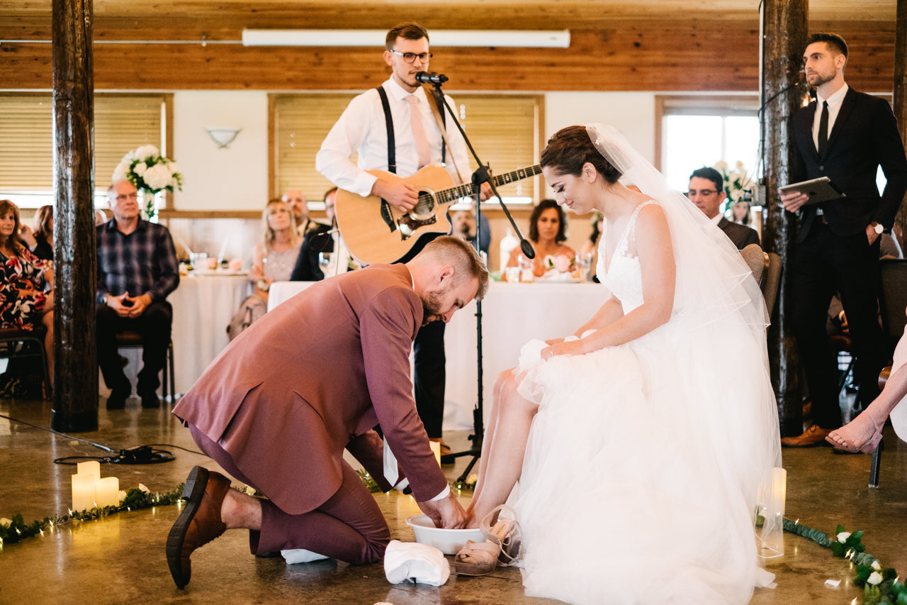 Feet washing ceremony during indoor wooden pavilion wedding while guitarist sings song 