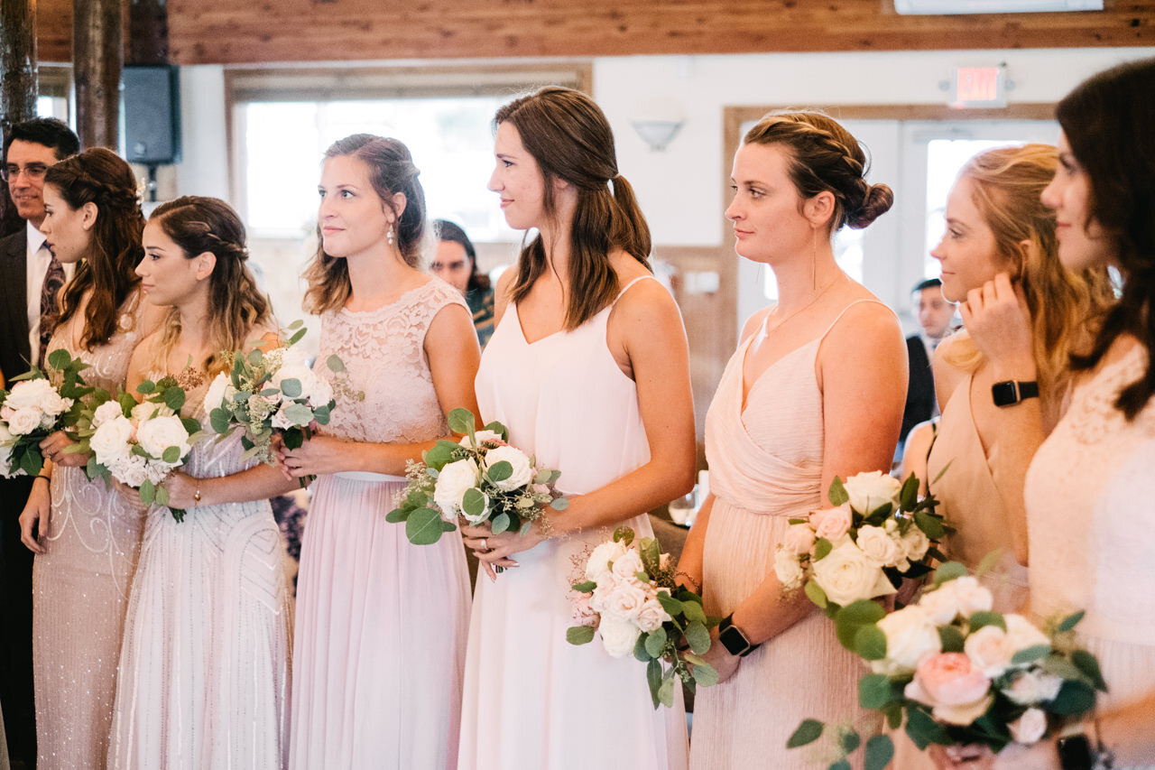  Bridesmaids in mismatched pink and peach dresses stand in line during wedding ceremony 