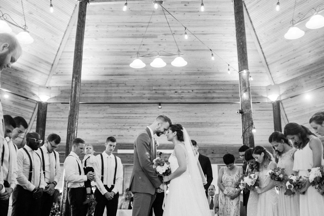  Bride and groom hold head together during prayer in wooden pavilion at cascade locks wedding 