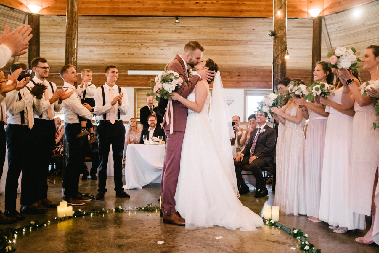  Bride and groom kiss during cascade locks ceremony while wedding party claps 