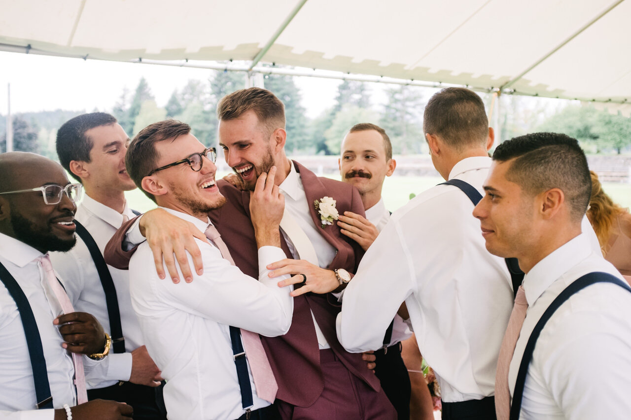  Groomsmen surround groom in purple suit as they hold his face 