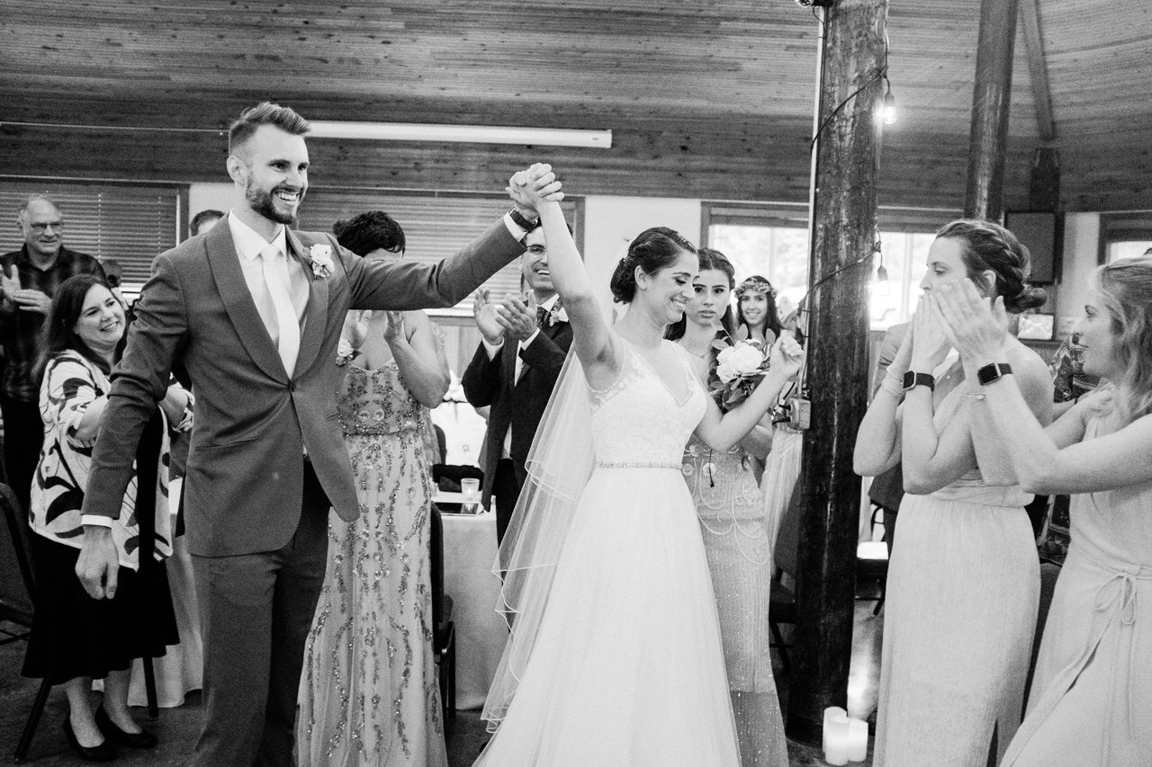  Bride and groom hold hands up while walking by guests to wedding table 