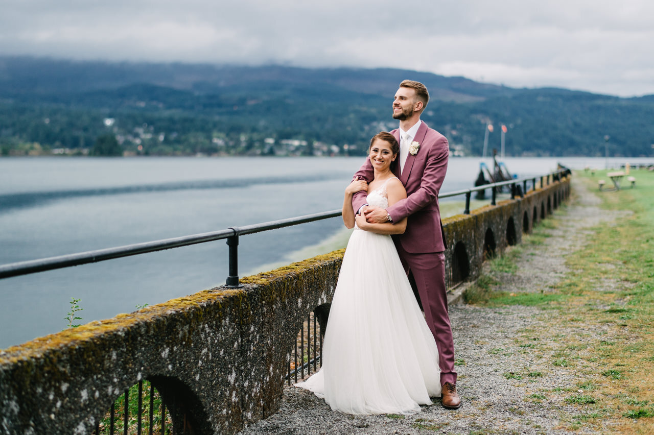  Groom holds bride by cascade locks marine Park in overcast day 