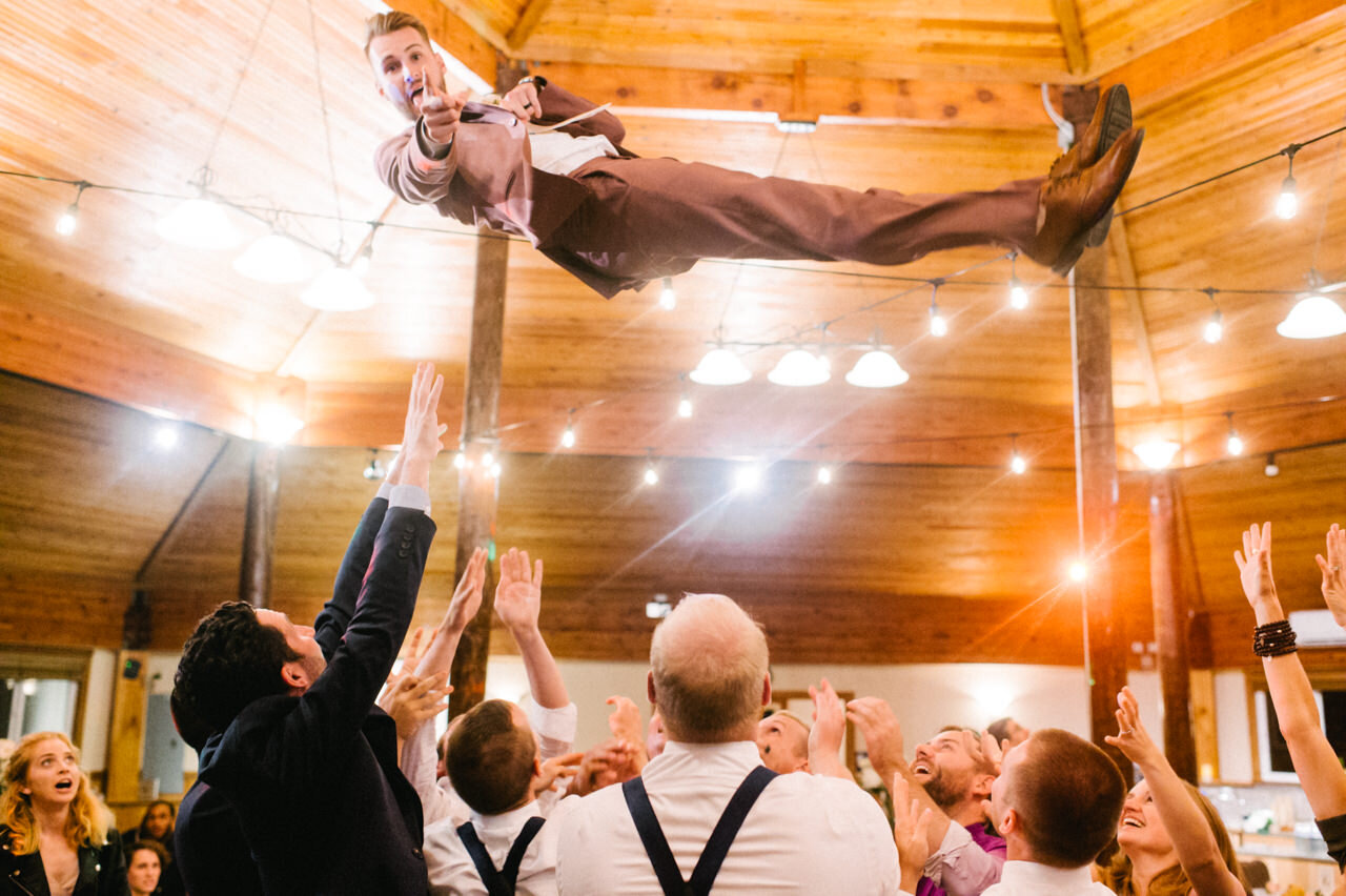  Groom in purple suit tossed in the air by groomsmen and points at the camera 