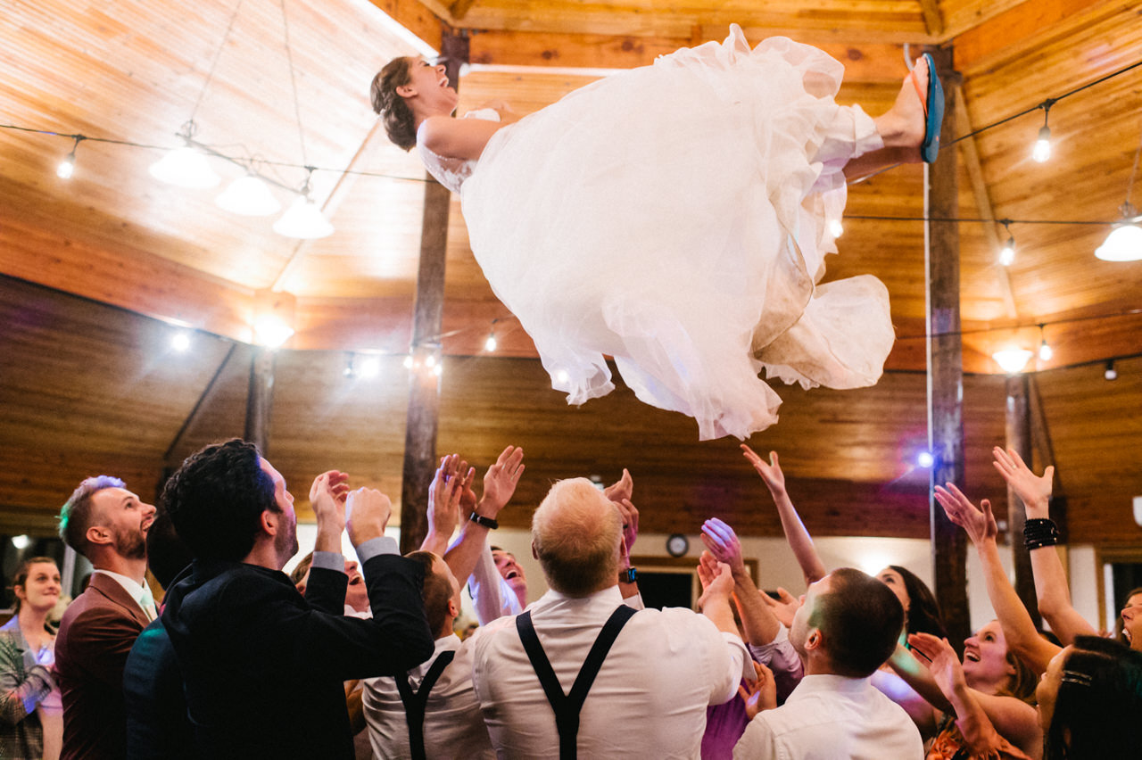  Bride in poofy wedding dress tossed high in the air at wooden pavilion 