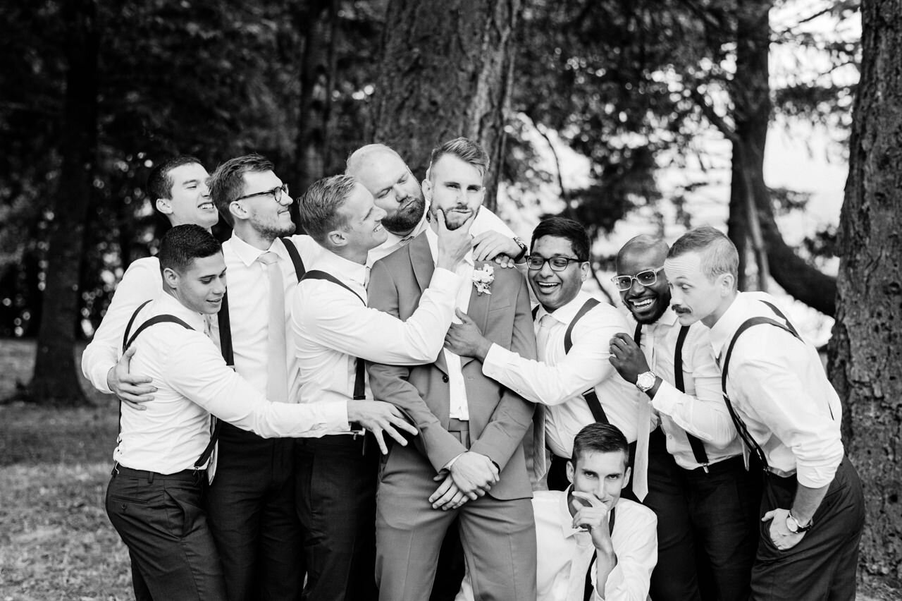  Funny portrait of groom and groomsmen as they fix his tie and hold his face 