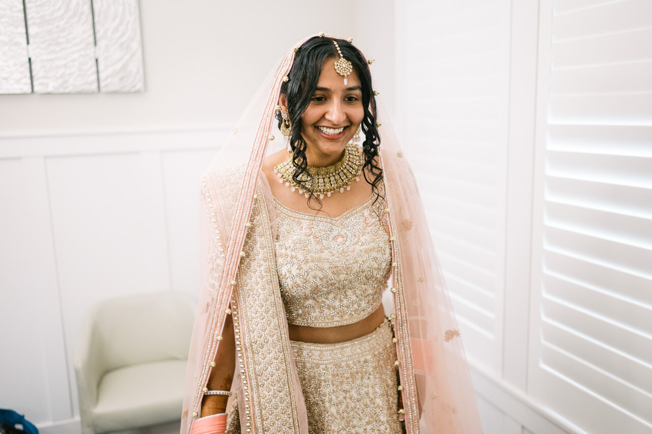  Bride dressed in indian sari with pink veil and gold and cream smiles 