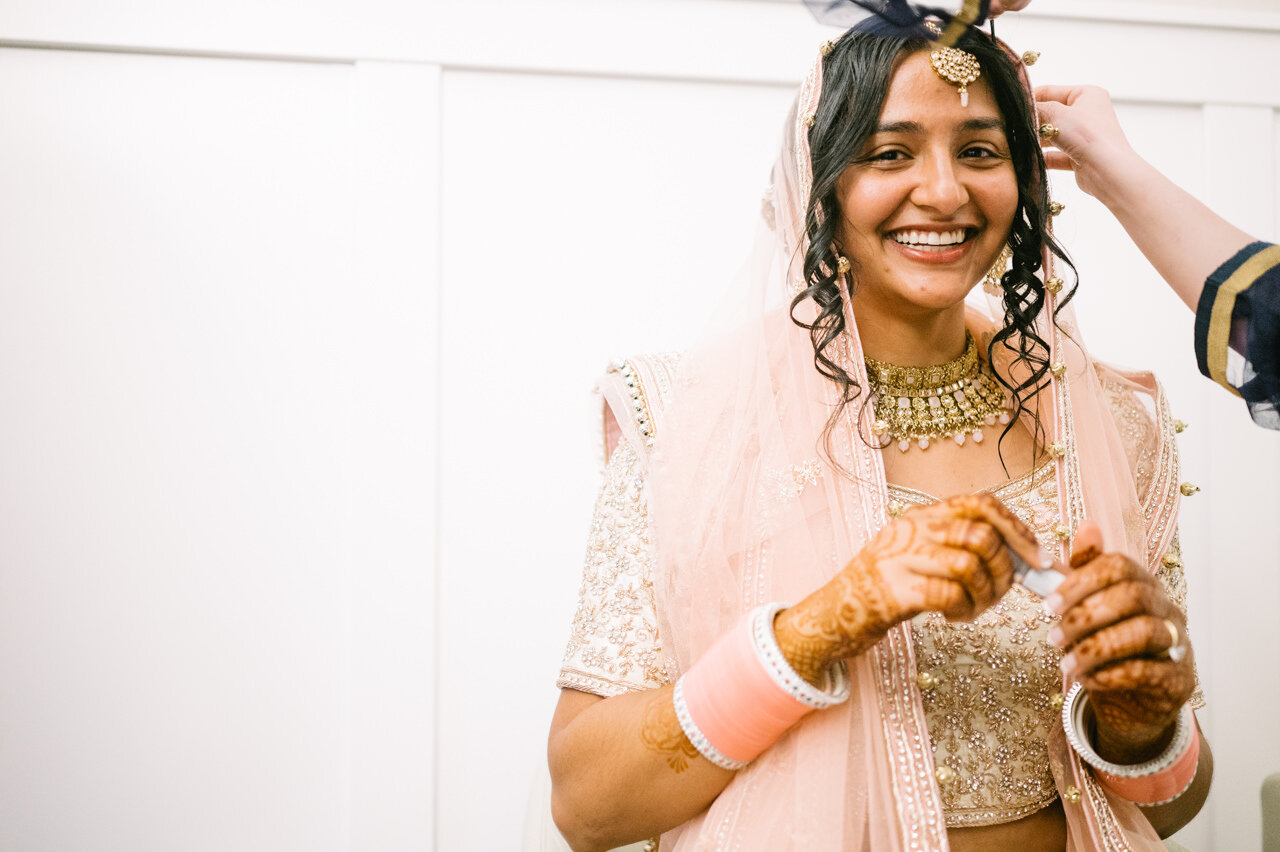  Indian bride in pink and gold sari smiles while getting ready 