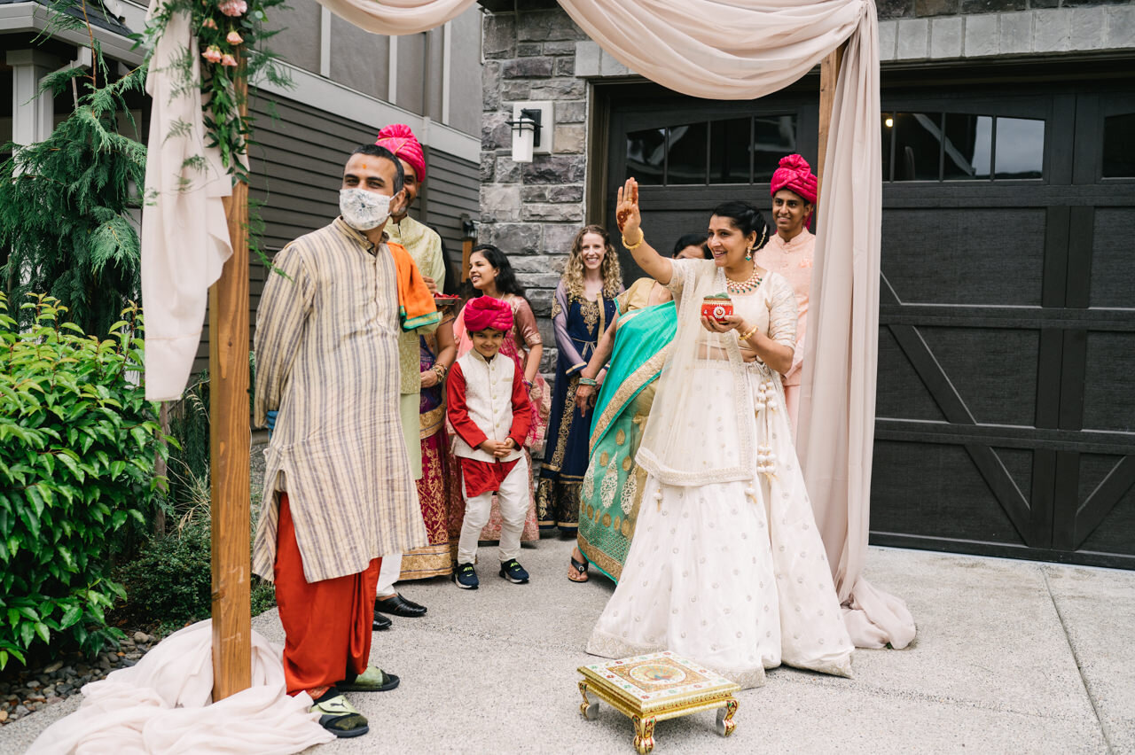  Indian bride's family waits for groom to arrive in front of residence and cream backdrop 