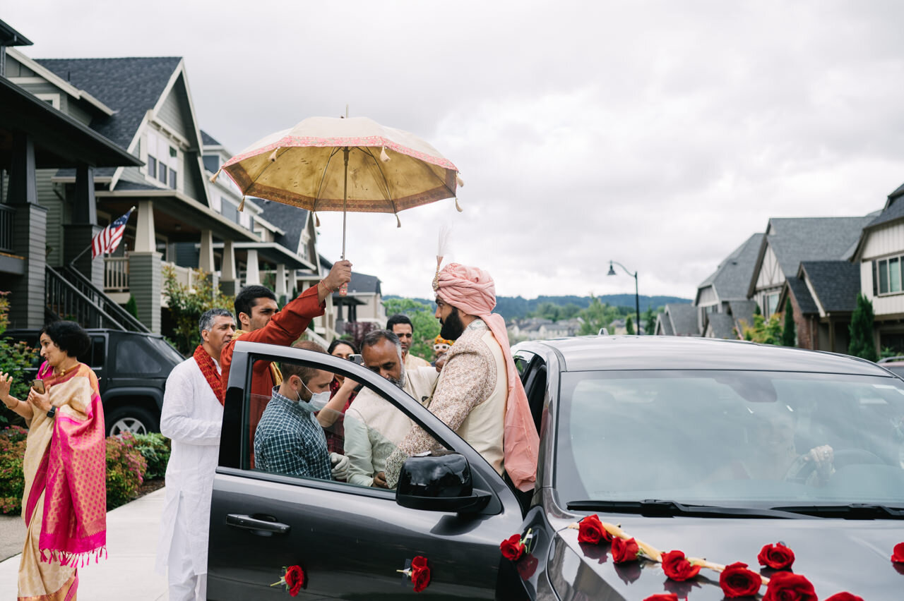  Grooms family hold umbrella for groom in pink and cream turban 