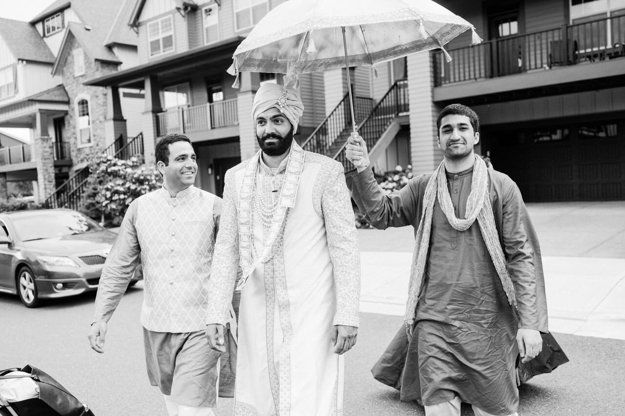  Groom crosses the street under umbrella with brothers 