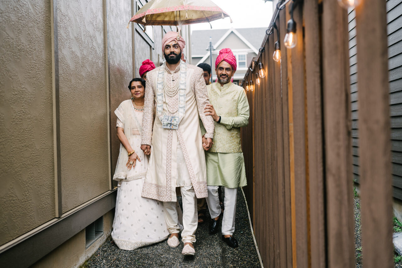  Groom arrives to wedding ceremony down backyard fence line holding bride family hands 