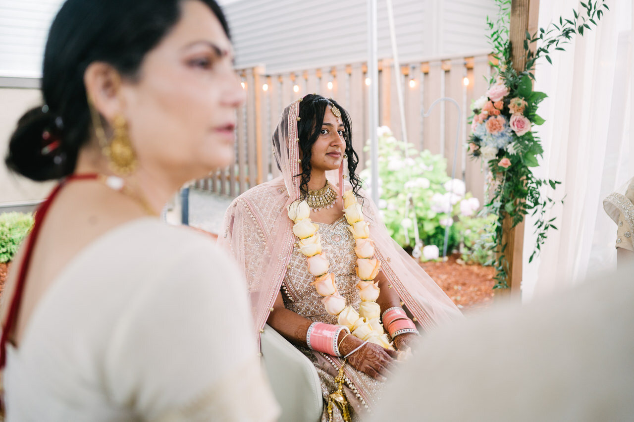  Indian bride waits in chair with yellow and pink rose necklace 