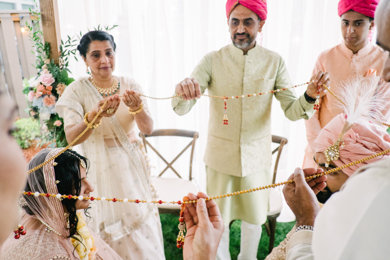  Parents hold beaded string around bride and groom under mandap 
