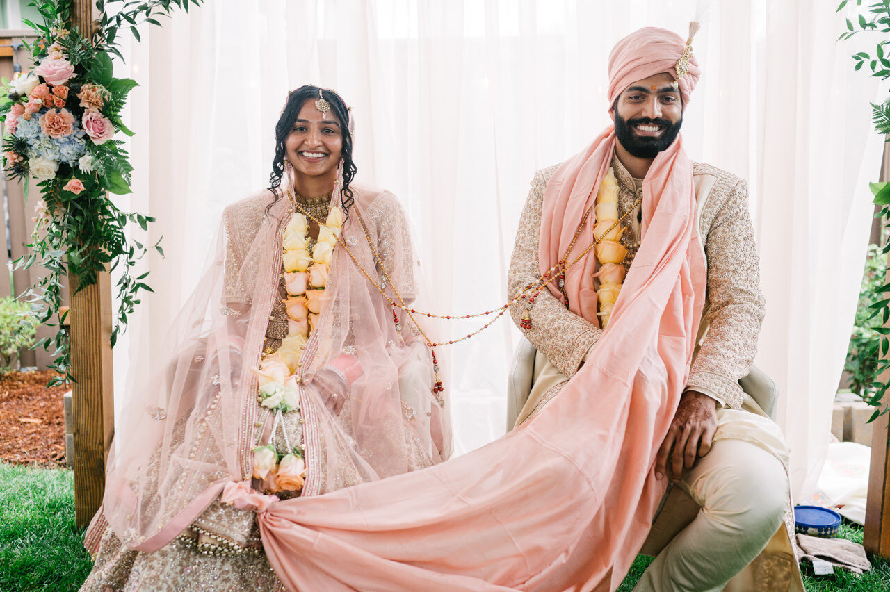  Bride and groom joined by pink cloth and beads under pink mandap 