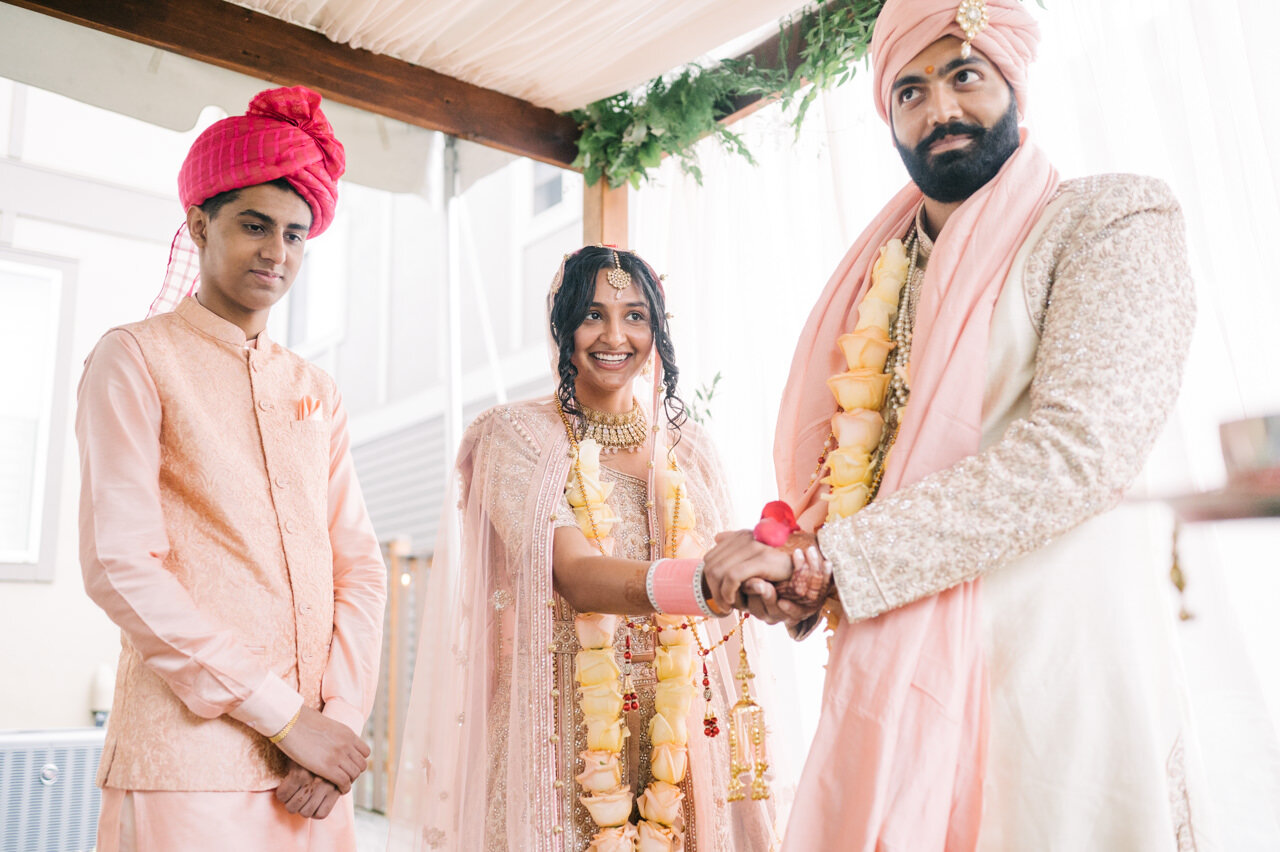 Bride and groom holding hands in indian wedding ceremony dressed in pink, cream, and gold 