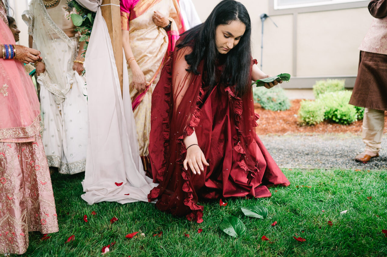  Placing leaves and flowers on ground, cousin dressed in red dress kneels 