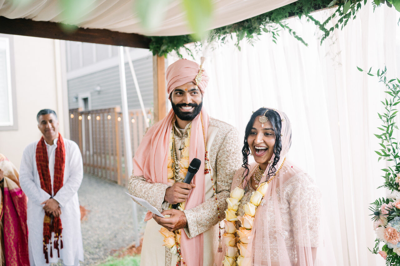  Bride and groom laugh under mandap while reading marriage notes 