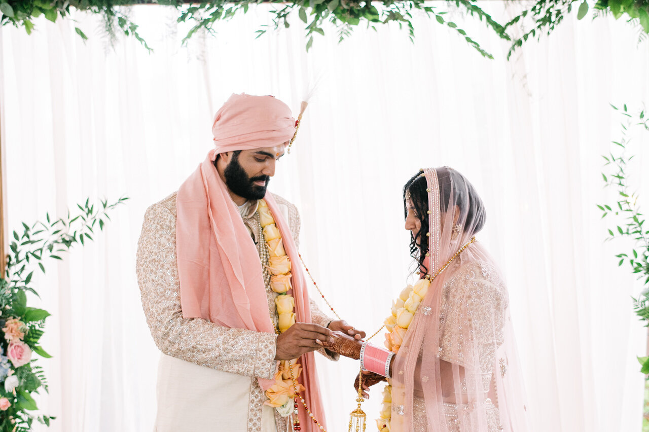  Indian Groom places ring on bride's hand dressed in pink and gold 