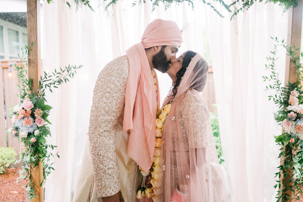  Bride and groom kiss under mandap with pink, cream, and yellow 