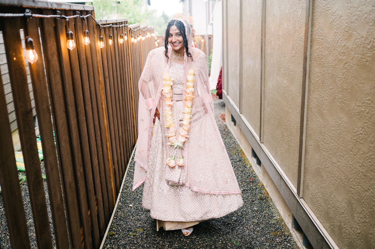  Bride walking down alley in pink, yellow and gold sari next to evening light bulbs 