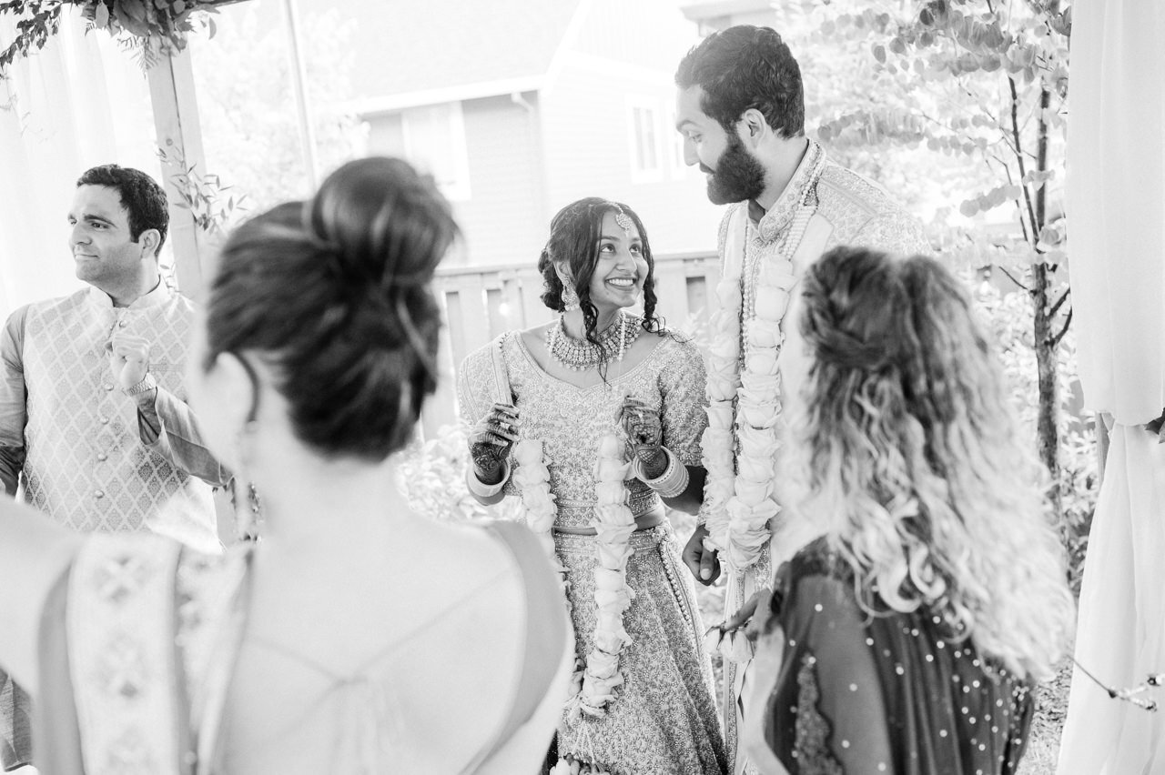  Bride smiling at groom while dancing in the backyard dressed in indian wedding attire 