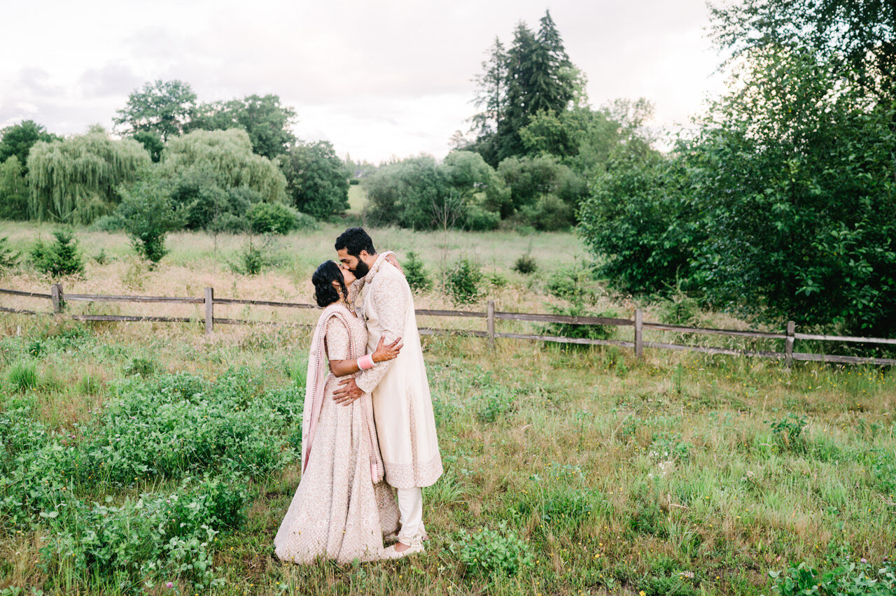  Bride and groom kiss in open field with fence line behind them 