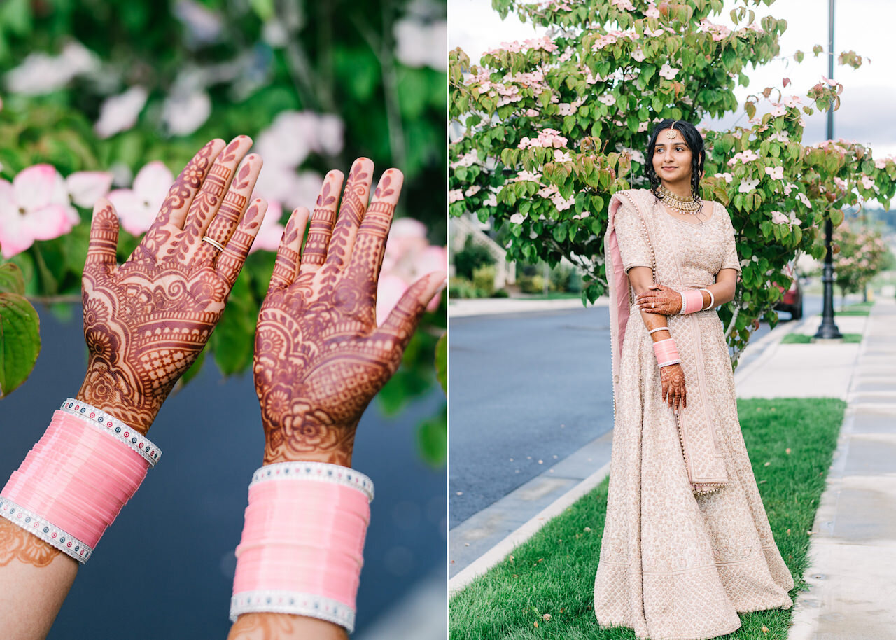  Bride stands in front of pink flowers while dressed in pink and gold, showing henna and bangles 