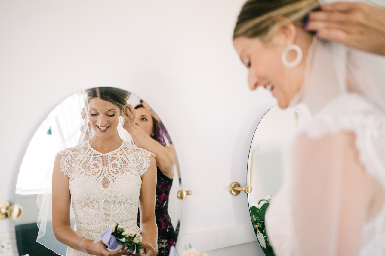  Bride having veil pinned on in mirror with lace wedding dress 