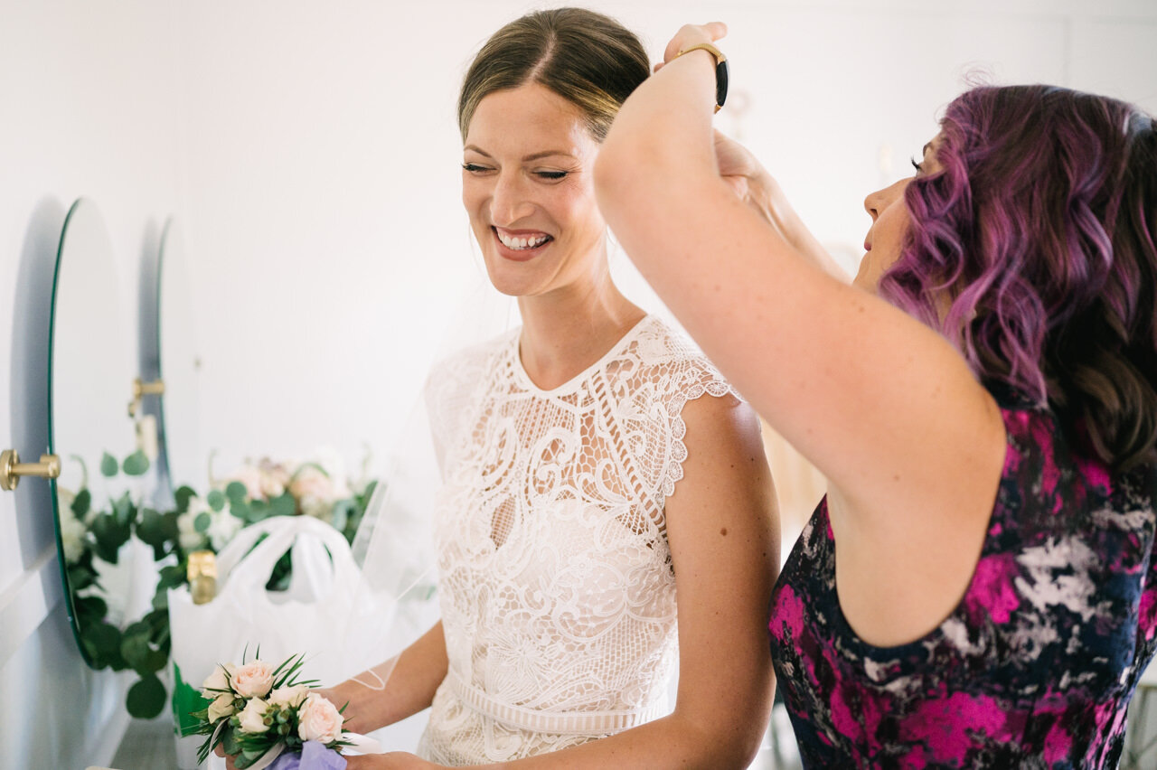  Bride laughing while maid of honor adjusts hair 