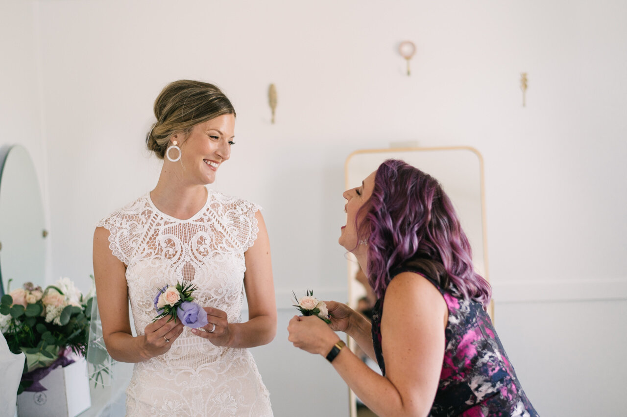  Bride and maid of honor with purple hair laugh while holding bouttainieres 