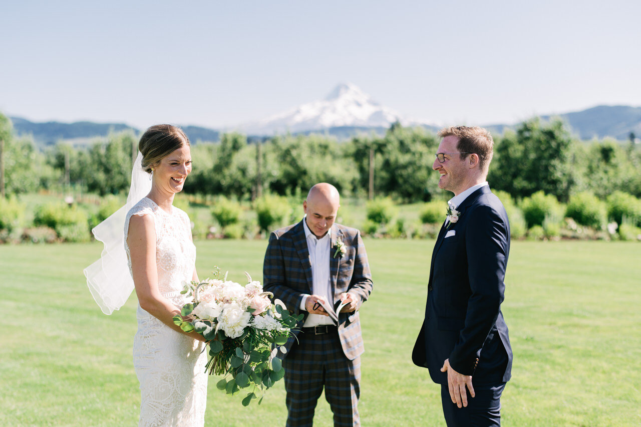  Bride and groom stand in lawn in front of mt hood on sunny day 
