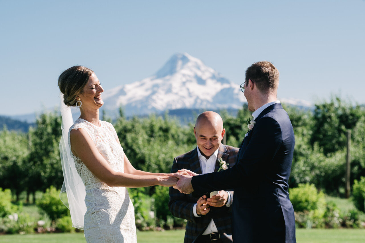  Bride laughs holding groom hands in front of mount hood 