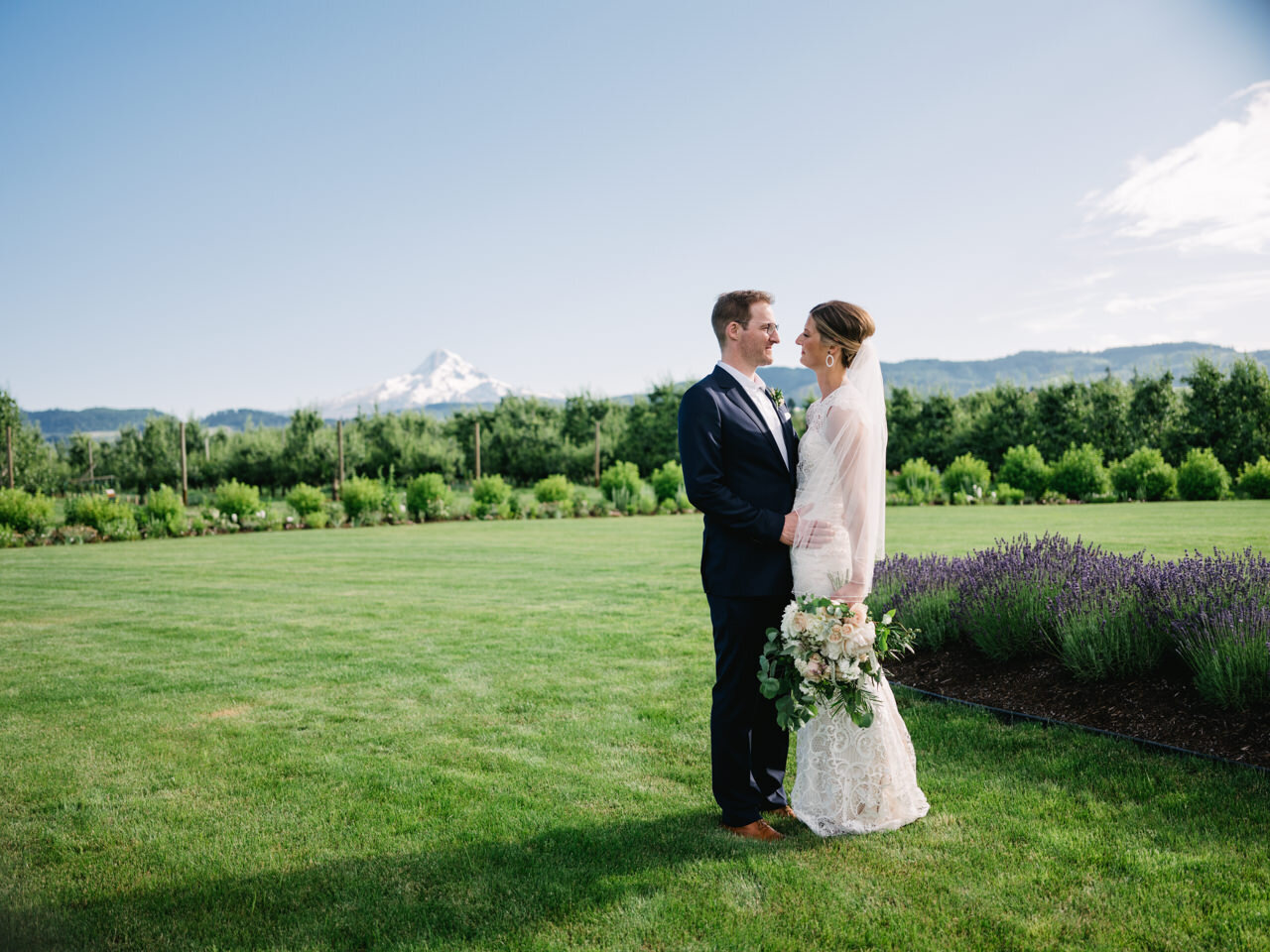  Bride and groom together in grass field with lavender in orchard before mt hood 