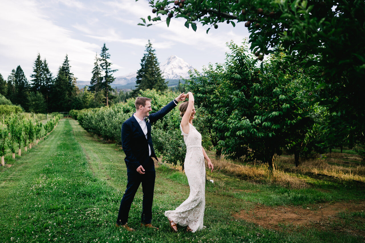  Groom spins bride in front of mt view orchard with mountain behind them 