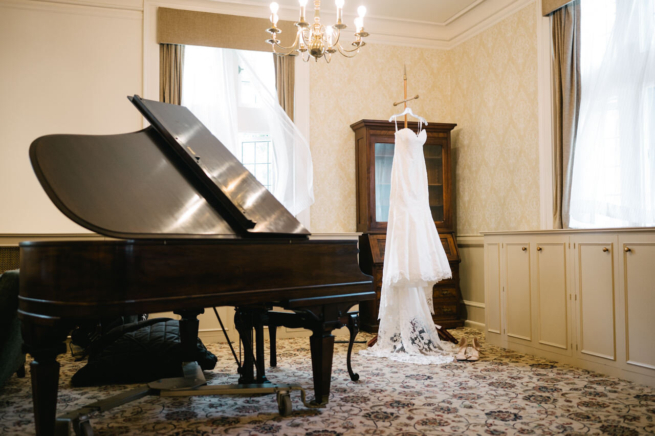  Wedding dress hanging by grand piano in ballroom 